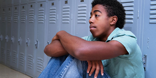 Depressed teenage boy, sitting against school lockers